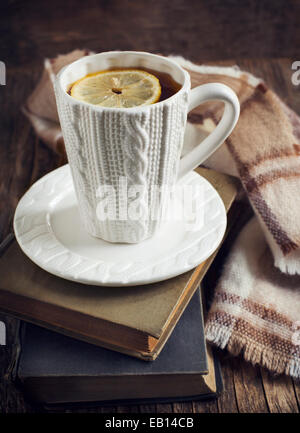 Tasse heißen Tee mit Zitrone, Buch und Schal auf Holztisch. Stockfoto