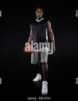Porträt von überzeugt junge Basketballspieler auf schwarzem Hintergrund. Afrikanische junger Mann hält einen Basketball Sportswear. Stockfoto