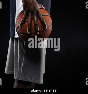 Bild eines jungen Mannes hält Basketball vor schwarzem Hintergrund abgeschnitten. Mitte Abschnitt Bild der afrikanischen Basketball-Spieler. Stockfoto