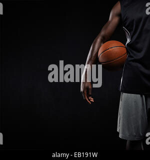 Zugeschnittenes Bild schwarze Basketballspieler stehend mit einem Basketball. Mann hält Basketball mit textfreiraum Sportswear. Stockfoto