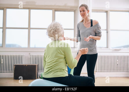 Physiotherapeuten nutzen für die Gesundheit, eine ältere Frau im Fitnessstudio zu erklären. Weibliche Trainer diskutieren Fortschritt mit ältere Frau am Stockfoto