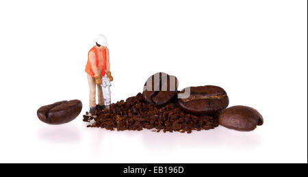 Miniatur-Arbeiter mit Powerdrill arbeitet an einer Kaffeebohne Stockfoto