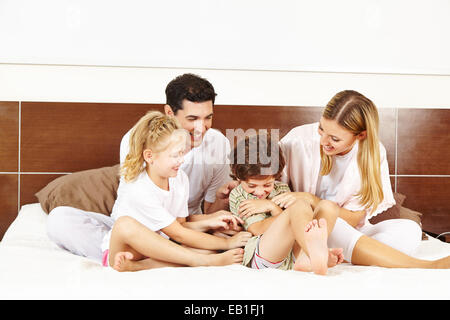 Glückliche Familie kitzeln ein Kind im Bett in einem Schlafzimmer Stockfoto