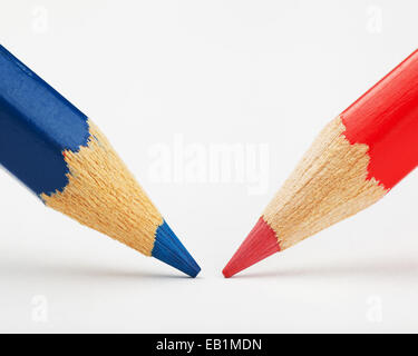 rote und blaue Stifte gegeneinander auf ein Blatt weißes Papier Stockfoto