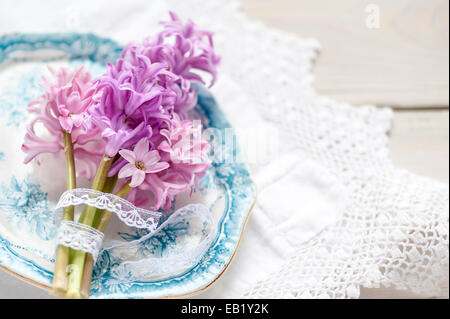 Posy rosa Hyazinthen auf Vintage blaue Platte auf Spitzen Tischdecke erschossen von oben Stockfoto