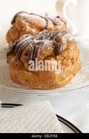 Choux Brötchen mit Creme gefüllt und mit Schokolade und Icing Sugar beträufelt Stockfoto