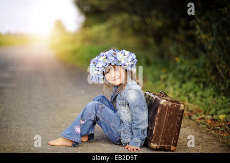 Fröhliche Mädchen sitzen auf der Straße, basierend auf einem Koffer Stockfoto