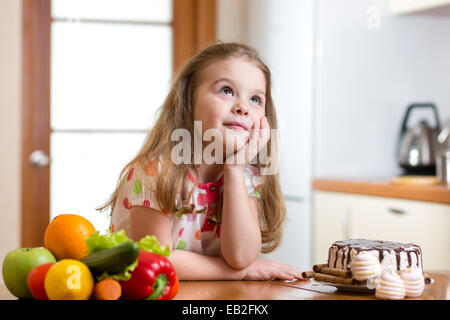 Kind die Wahl zwischen gesundes Gemüse und leckere Süßigkeiten Stockfoto