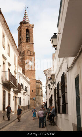 Kirche der Muttergottes von der Übernahme und Menschen in Dorfstraße, Aroche, Sierra de Aracena, Provinz Huelva, Spanien Stockfoto