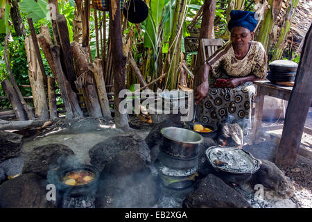 Eine Frau kocht traditionelle afrikanische Gerichte aus Kartoffeln, Fleisch und Gemüse in einer Dorf-Küche. Stockfoto