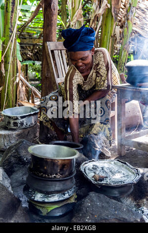 Eine Frau, eine traditionelle afrikanische Mahlzeit aus Kartoffeln, Fleisch und Gemüse in einer Dorf-Küche kochen. Stockfoto