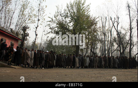 Srinagar, Kaschmir. 25. November 2014. Kaschmiris stehen in Warteschlange wie indische Secuirty Stabds schützen ihre Stimmen vor einem Wahllokal in der ersten Phase der Abstimmung der Jammu und Kaschmir Zustand Versammlung Wahlen am Rakh Shilvat, Stadtrand von Srinagar, kontrolliert indischen Kaschmir. Tausende standen Schlange, um ihre Stimmen inmitten einem Boykott-Aufruf von muslimischen separatistischen Gruppen, die über die umstrittenen Himalaya-Region Indiens Souveränität ablehnen. Bildnachweis: Sofi Suhail/Alamy Live-Nachrichten Stockfoto