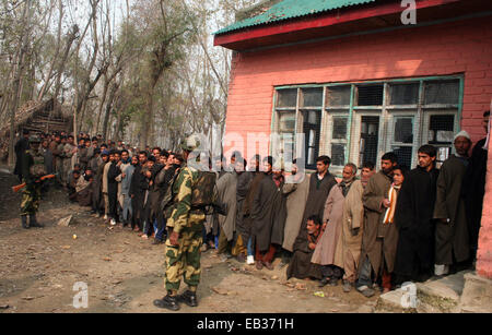 Srinagar, Kaschmir. 25. November 2014. Kaschmiris stehen in Warteschlange wie indische Secuirty Stabds schützen ihre Stimmen vor einem Wahllokal in der ersten Phase der Abstimmung der Jammu und Kaschmir Zustand Versammlung Wahlen am Rakh Shilvat, Stadtrand von Srinagar, kontrolliert indischen Kaschmir. Tausende standen Schlange, um ihre Stimmen inmitten einem Boykott-Aufruf von muslimischen separatistischen Gruppen, die über die umstrittenen Himalaya-Region Indiens Souveränität ablehnen. Bildnachweis: Sofi Suhail/Alamy Live-Nachrichten Stockfoto