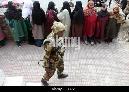 Srinagar, Kaschmir. 25. November 2014. Kaschmiris stehen in Warteschlange wie indische Secuirty Stabds schützen ihre Stimmen vor einem Wahllokal in der ersten Phase der Abstimmung der Jammu und Kaschmir Zustand Versammlung Wahlen am Bandipora, Stadtrand von Srinagar, kontrolliert indischen Kaschmir. Tausende standen Schlange, um ihre Stimmen inmitten einem Boykott-Aufruf von muslimischen separatistischen Gruppen, die über die umstrittenen Himalaya-Region Indiens Souveränität ablehnen. Bildnachweis: Sofi Suhail/Alamy Live-Nachrichten Stockfoto