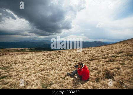 Junger Mann mit roten Pullover sitzen verdorrten Rasen fotografieren Stockfoto