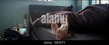 Nahaufnahme der Füße einer Person im Bett, die unter einer Bettdecke herausragen Stockfoto