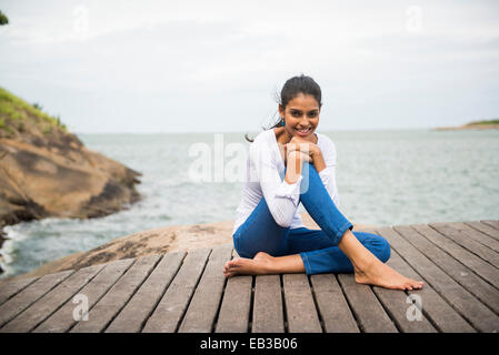 Frau sitzt auf der Holzterrasse mit Blick auf See Stockfoto