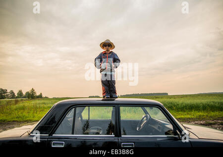 Kaukasische Junge stand auf Autodach im ländlichen Bereich Stockfoto