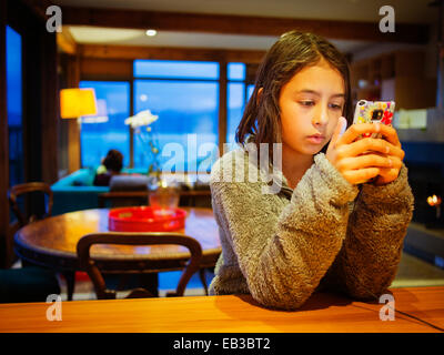 Gemischte Rassen Mädchen mit Handy am Tisch Stockfoto