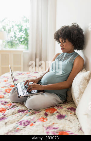 Schwanger African American Mutter mit Laptop-Computer im Bett Stockfoto