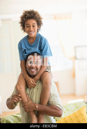 Vater mit Sohn auf Schultern im Wohnzimmer Stockfoto