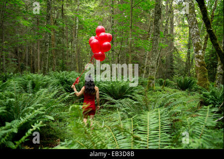 Koreanische Frau mit roten Luftballons in üppigen Wald Stockfoto