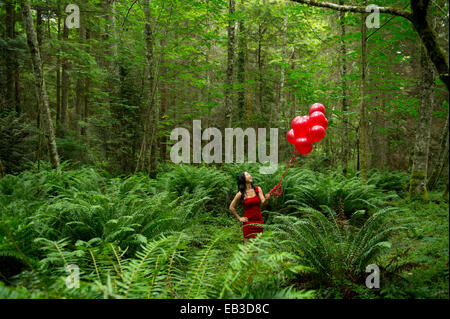 Koreanische Frau mit roten Luftballons in üppigen Wald Stockfoto