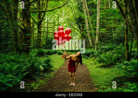 Koreanische Frau mit roten Luftballons in üppigen Wald Stockfoto