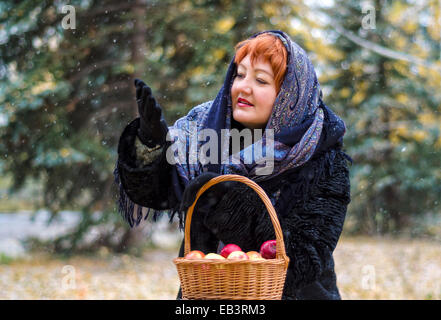 Frau mit Korb Äpfel im Wald, kommt den ersten Schnee Stockfoto