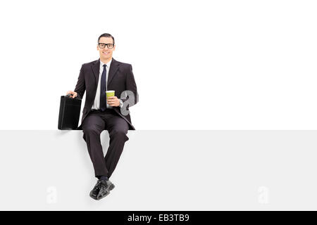 Geschäftsmann hält eine Tasse Kaffee sitzen auf einer leeren Platte isoliert auf weißem Hintergrund Stockfoto