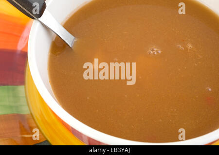 Eine Schüssel Hühnersuppe in einer Tomaten-Suppe mit Löffel auf einem bunten Teller. Stockfoto