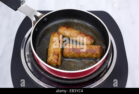 Drei Frühstück Würstchen braten in einer kleinen Pfanne auf einem einzigen Brenner Gasherd. Stockfoto