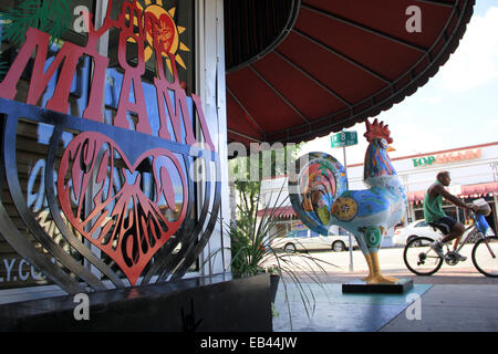 Ein Radfahrer geht eine hölzerne Skulptur von einem Hahn im Stadtteil Little Havana von Miami, Florida. Stockfoto