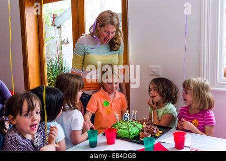 Ein Junge Ausblasen der Kerzen auf seine Torte auf seiner Geburtstagsparty, umgeben von seinen Freunden. Stockfoto