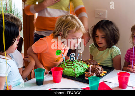 Ein Junge Ausblasen der Kerzen auf seine Torte auf seiner Geburtstagsparty, umgeben von seinen Freunden. Stockfoto