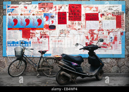 traditionelle Fahrrad- und moderne Moped vor Wand bedeckt in Plakaten in china Stockfoto