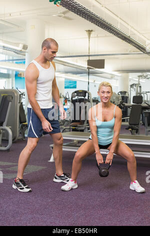 Trainer unterstützen Frau mit Wasserkocher Glocke im Fitness-Studio Stockfoto