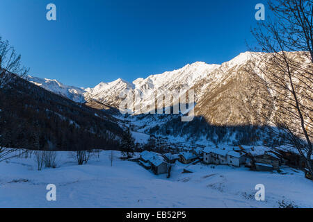 Winterlandschaft bei Sonnenaufgang über Alpental und kalten schneebedeckten Dorf im Skigebiet Praly, Piemont, italienischen Alpen. Stockfoto