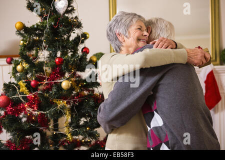 Älteres paar umarmt neben ihren Weihnachtsbaum Stockfoto