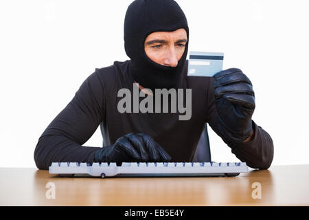 Einbrecher auf Tastatur tippen und halten Sie Kreditkarte Stockfoto