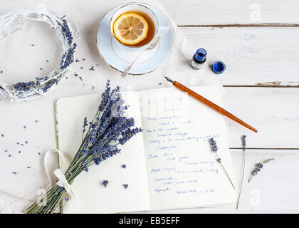 Overhead Schuss aus einem Haufen von Lavendel auf einem Notebook mit Handschrift, auf weißen Tisch, mit Feder, Tinte, Kranz und Teetasse Stockfoto