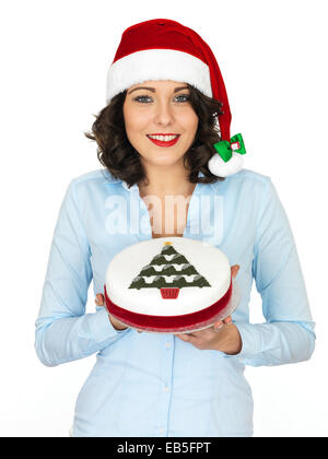 Selbstbewussten jungen Frau trägt eine rote Weihnachtsmütze Holding ein reichhaltiges Iced Weihnachten Fruit Cake Isoliert gegen einen weißen Hintergrund mit einen Freistellungspfad Stockfoto