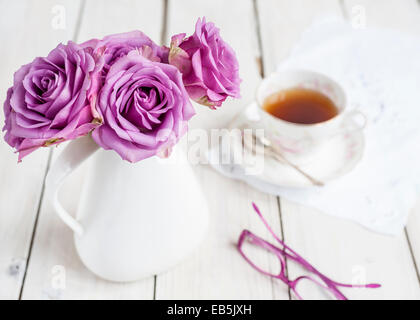 Teepause - rosa Rosen in weißem Krug auf weißen Tisch, Vintage Teetasse und Gläser - unscharfen Hintergrund Stockfoto