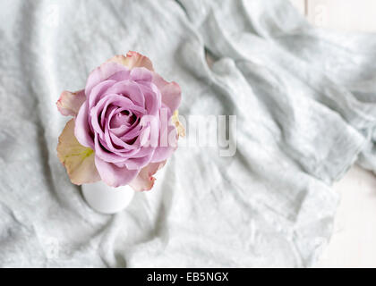 Einzelne lila Rose in einer weißen Vase mit grauer Seide Stoff im Hintergrund Stockfoto
