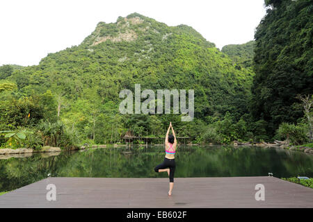 Eine Frau praktiziert Yoga neben einem natürlich beheizten Pool auf dem Banjaran Hotspring Rückzug in der Nähe von Ipoh, Malaysia. Stockfoto