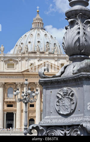 Nahaufnahme einer päpstlichen Wappen auf der Basis von einem Laternenmast auf dem Vatikan Platz und die Basilika St. Peter hinter in Rom, Italien. Stockfoto