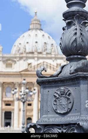 Nahaufnahme einer päpstlichen Wappen auf der Basis von einem Laternenmast auf dem Vatikan Platz und die Basilika St. Peter hinter in Rom, Italien. Stockfoto