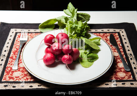 Rohe frische Radieschen auf einem weißen Teller mit einer Gabel und einem Messer Stockfoto