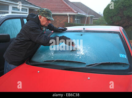 Ein älterer Mann Schaben Frost aus einem Auto Windschutzscheibe an einem frostigen Morgen. Stockfoto