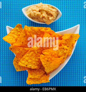 eine Platte mit Tortilla-Chips und eine Schüssel mit Hummus, auf einem blauen Hintergrund Stockfoto